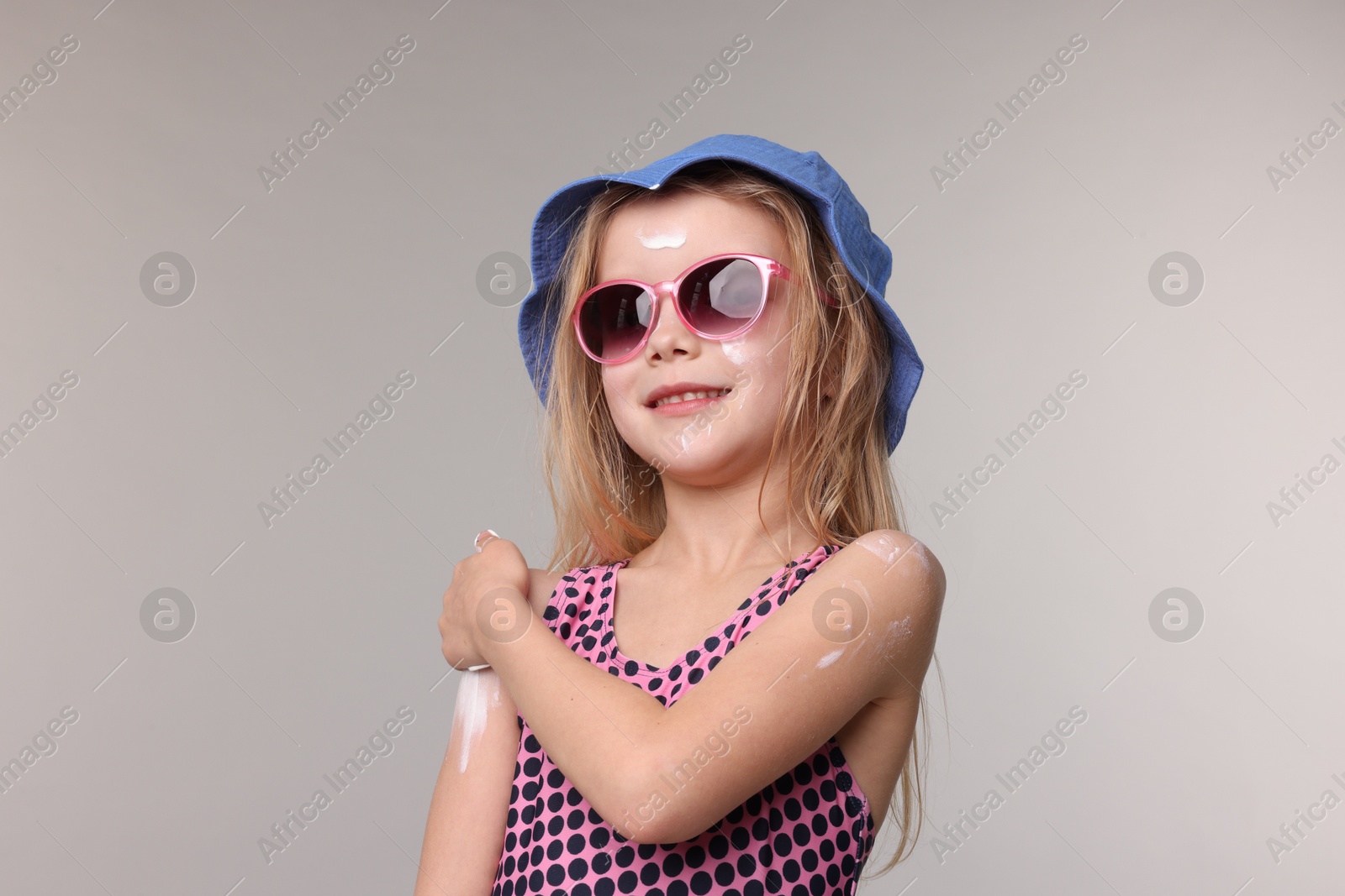 Smiling little girl applying sun protection product onto her shoulder on grey background Photo of Smiling little girl applying sun protection product onto her shoulder on grey background