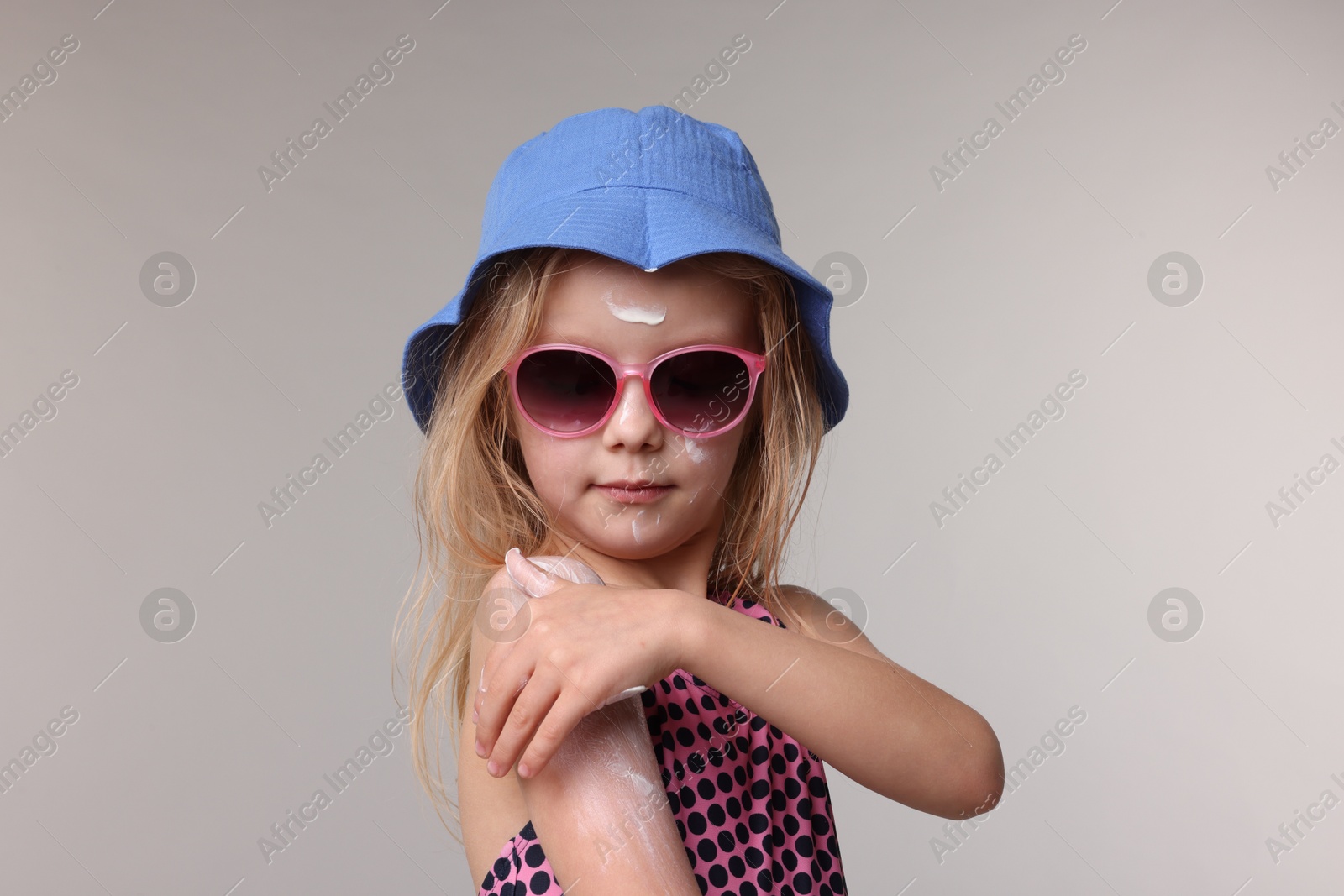 Photo of Cute little girl applying sun protection product onto her shoulder on grey background