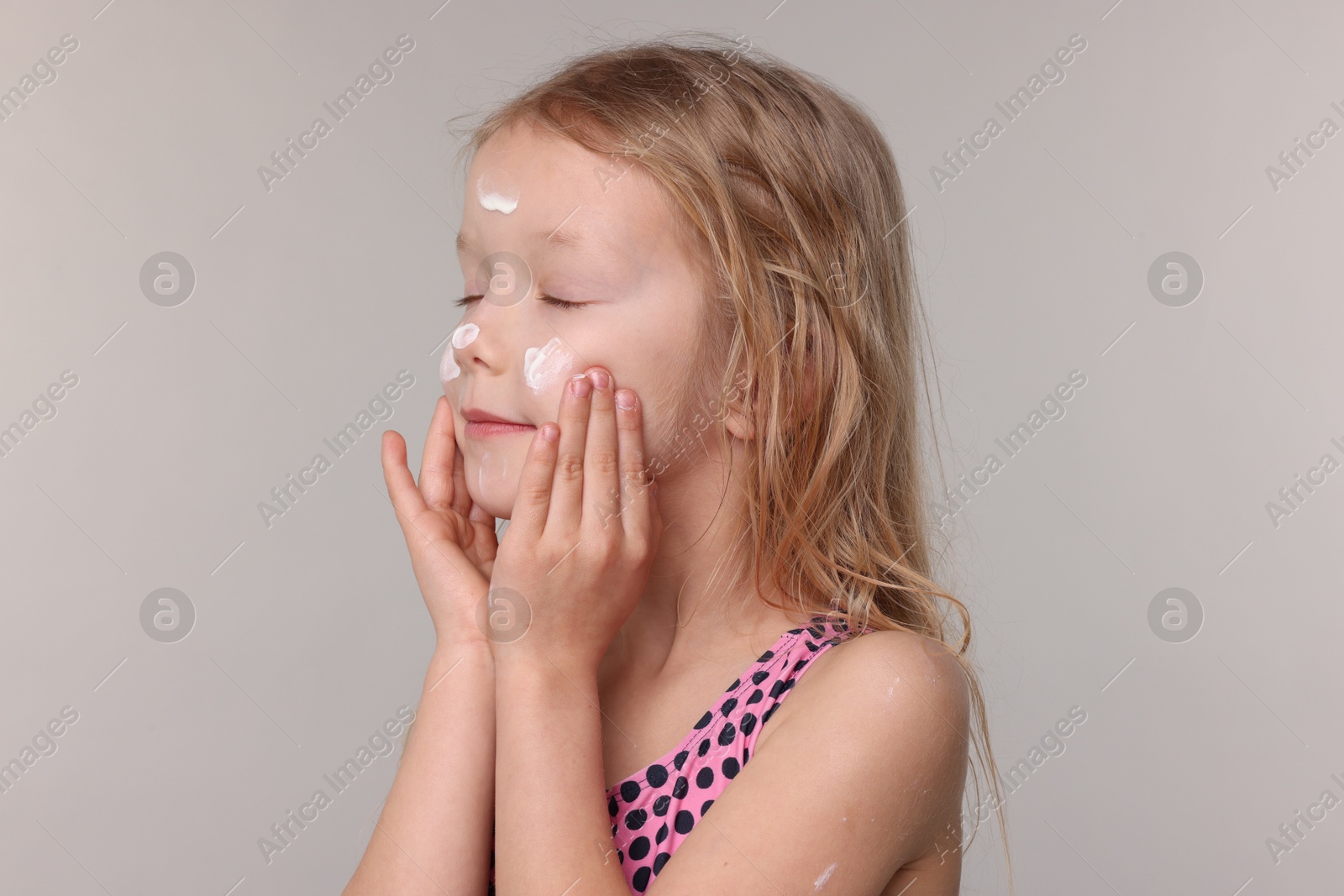 Cute little girl applying sun protection product onto her face on grey background, closeup Photo of Cute little girl applying sun protection product onto her face on grey background, closeup