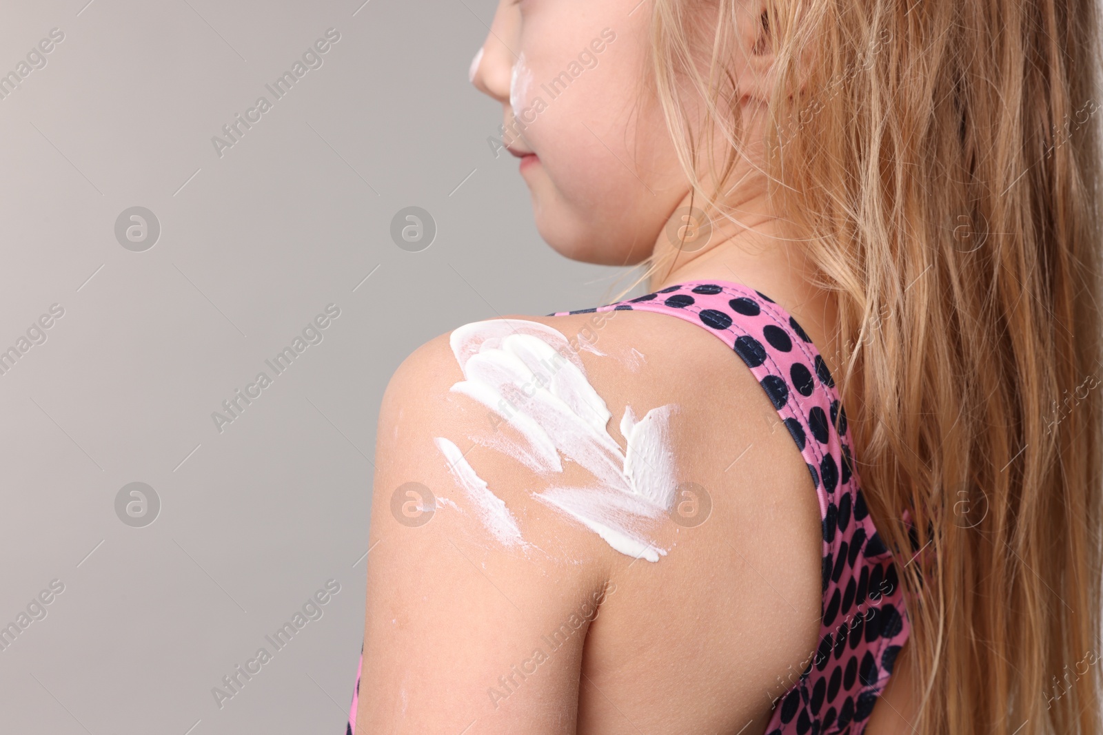 Photo of Little girl with sun protection cream on her skin against grey background, back view. Space for text
