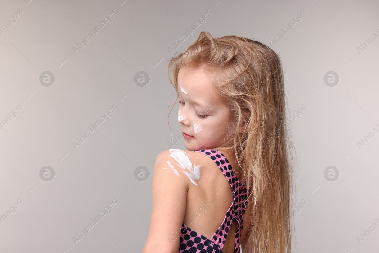 Photo of Cute little girl with sun protection cream on her skin against grey background, back view. Space for text