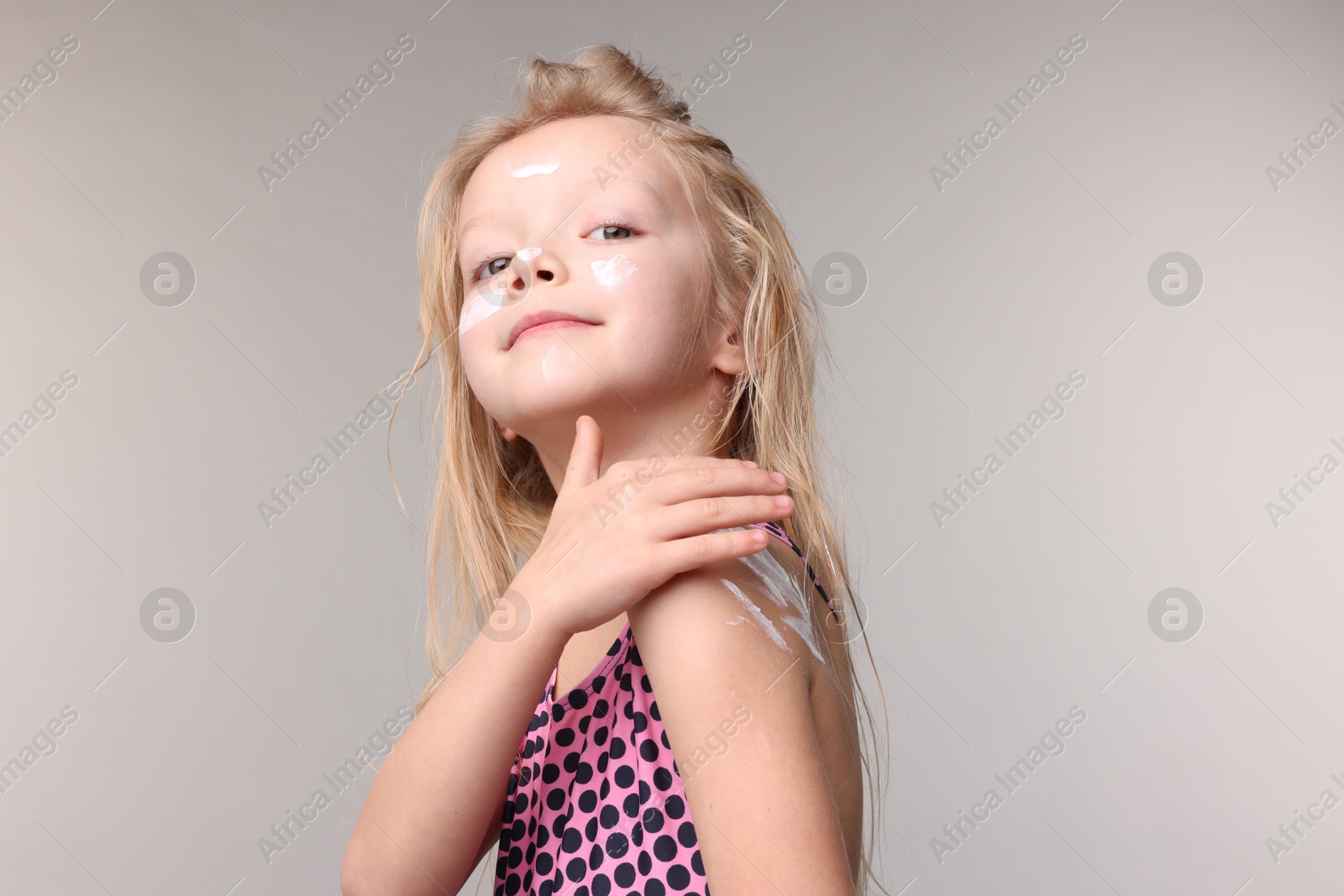 Cute little girl applying sun protection product onto her shoulder on grey background Photo of Cute little girl applying sun protection product onto her shoulder on grey background