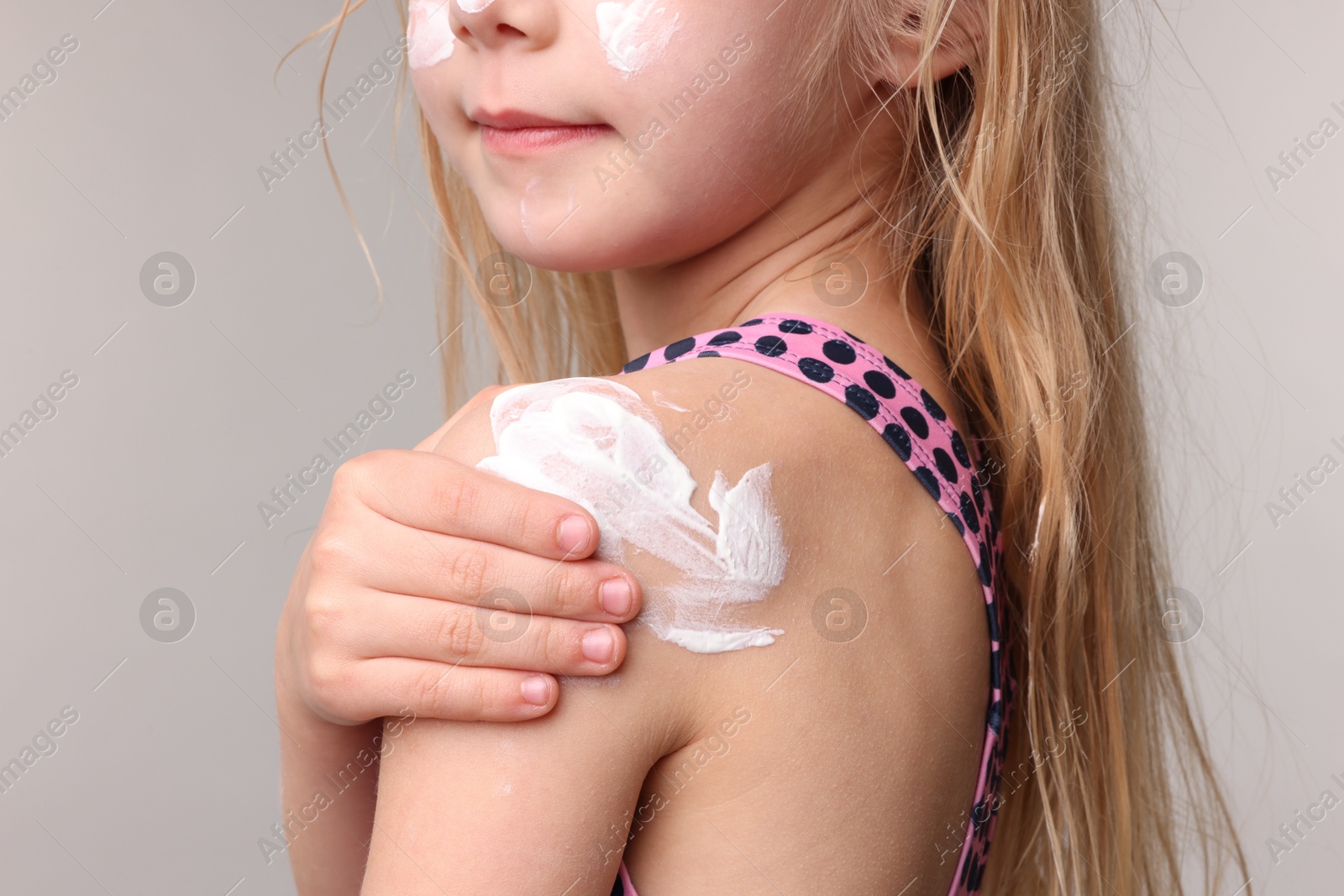 Photo of Little girl with sun protection cream on her skin against grey background, closeup