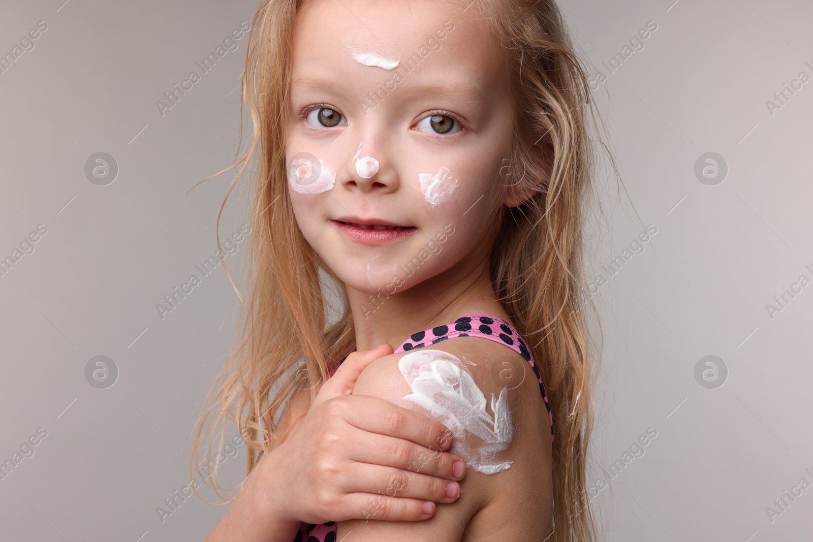 Cute little girl applying sun protection product onto her shoulder on grey background, closeup Photo of Cute little girl applying sun protection product onto her shoulder on grey background, closeup