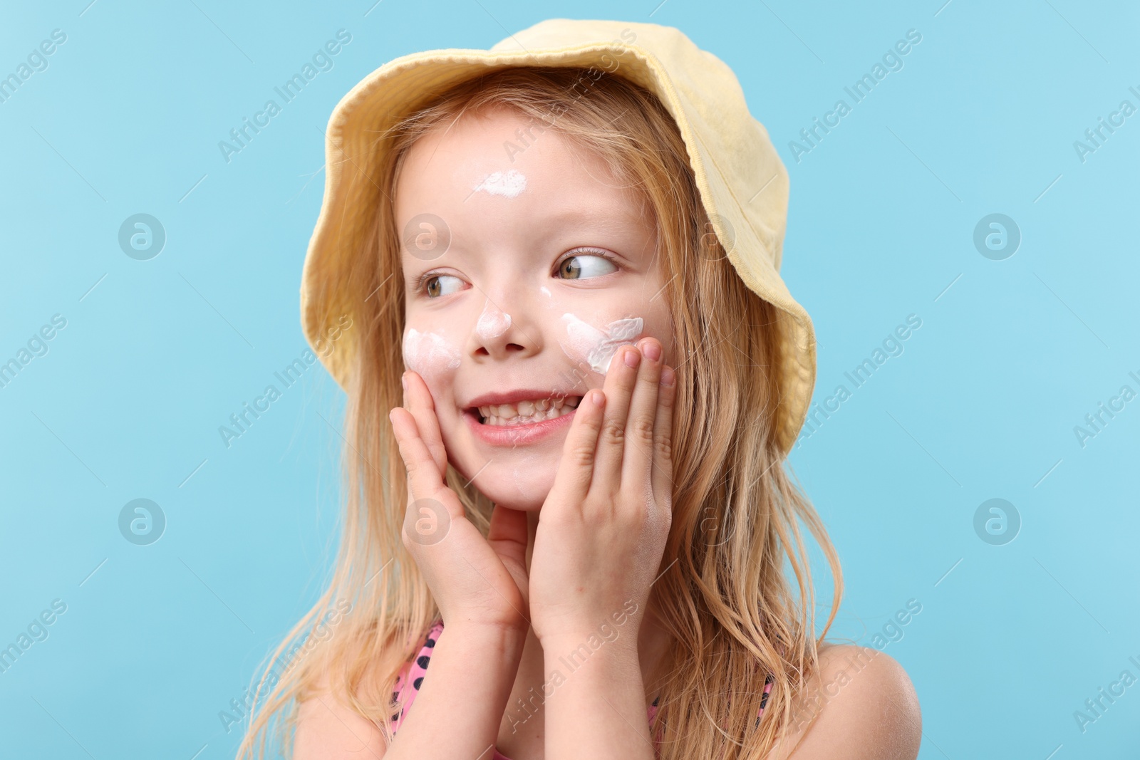 Smiling little girl with sun protection cream on her face against light blue background Photo of Smiling little girl with sun protection cream on her face against light blue background