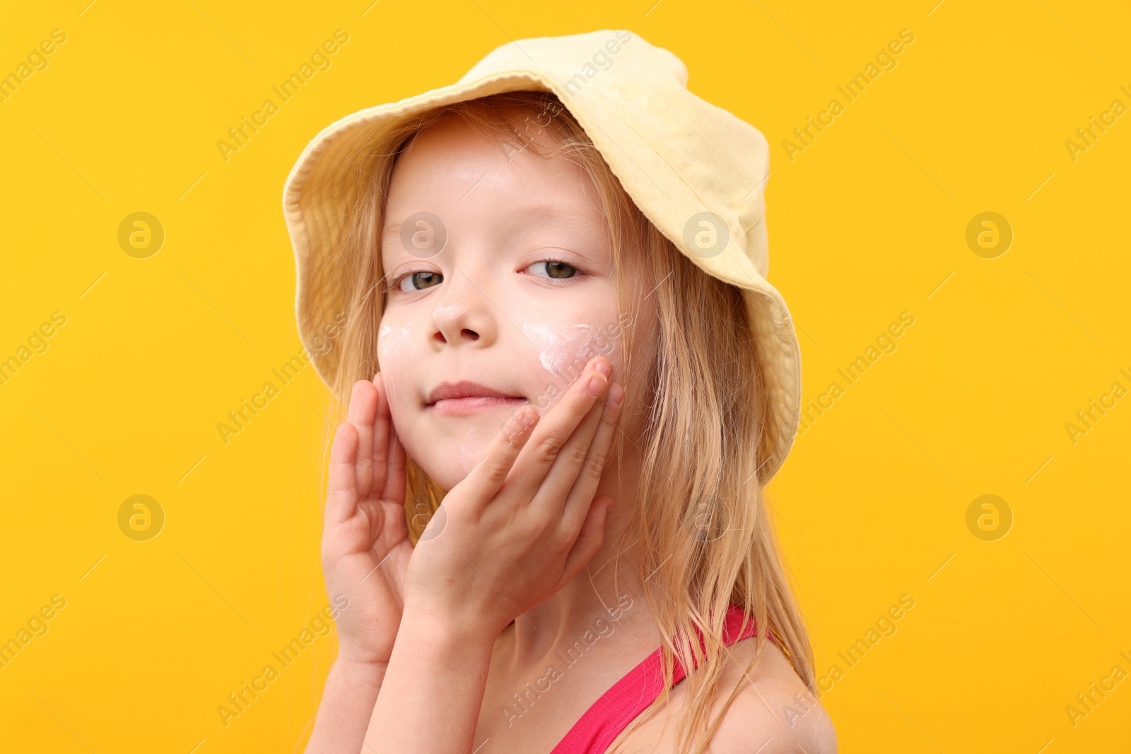 Cute little girl applying sun protection cream onto her face against yellow background, closeup Photo of Cute little girl applying sun protection cream onto her face against yellow background, closeup