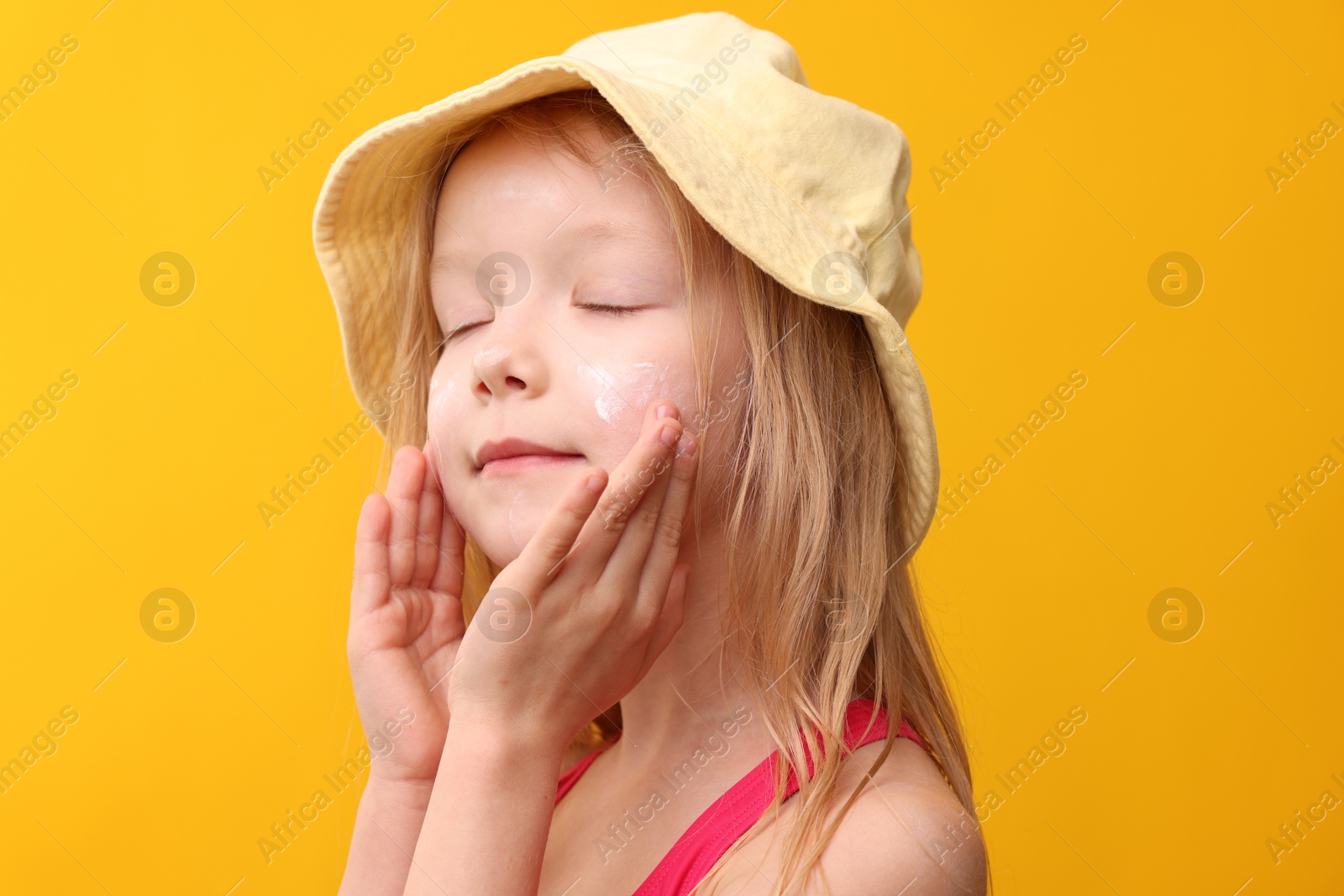 Cute little girl applying sun protection cream onto her face against yellow background, closeup Photo of Cute little girl applying sun protection cream onto her face against yellow background, closeup