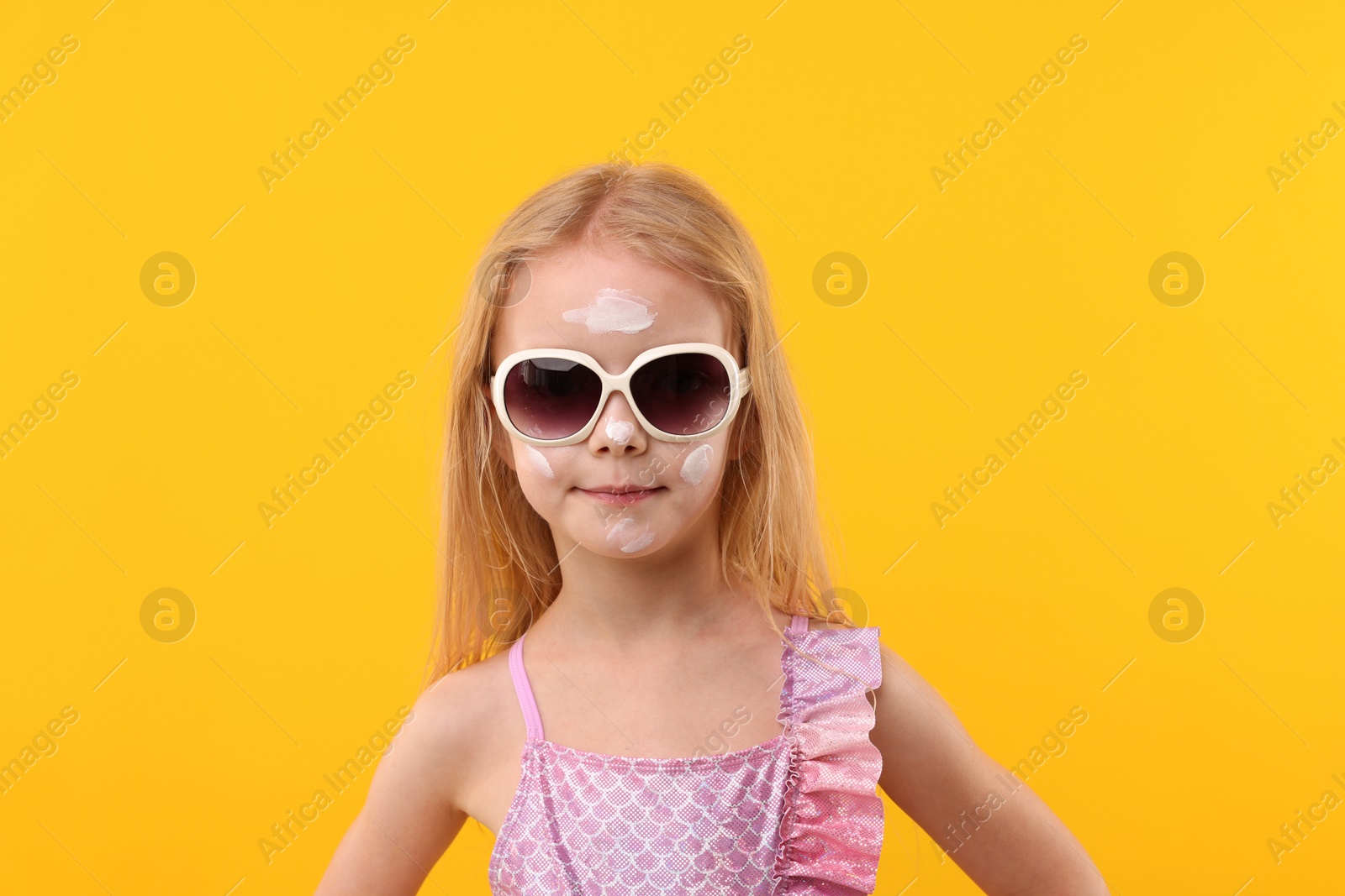 Photo of Cute little girl with sun protection cream on her face against yellow background