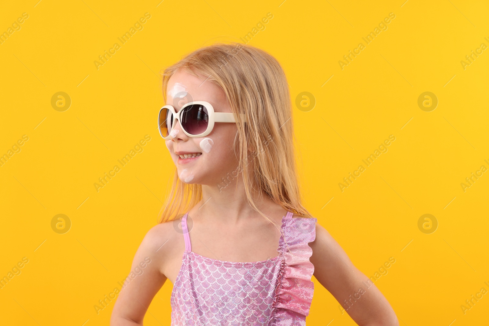 Photo of Smiling little girl with sun protection cream on her face against yellow background