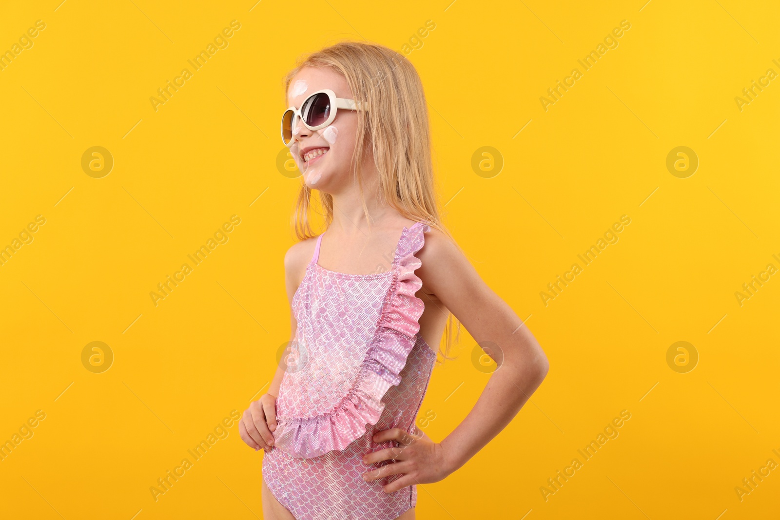 Smiling little girl with sun protection cream on her face against yellow background Photo of Smiling little girl with sun protection cream on her face against yellow background