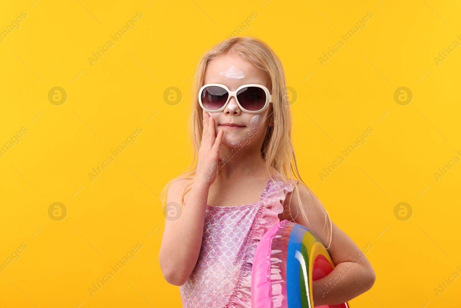 Photo of Cute little girl with sun protection cream on her face against yellow background
