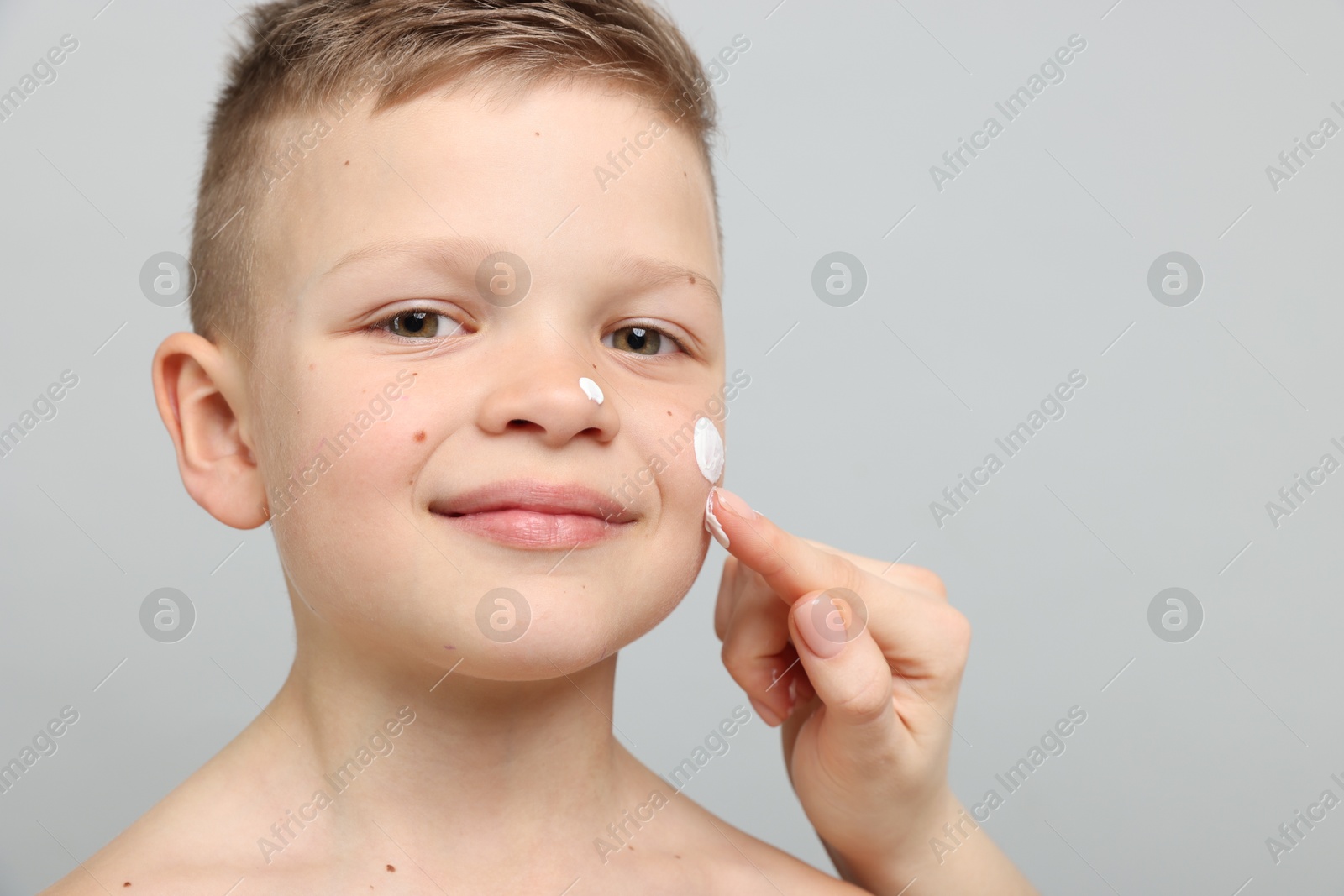 Mother applying sun protection cream onto her son's skin on light grey background, closeup Photo of Mother applying sun protection cream onto her son's skin on light grey background, closeup