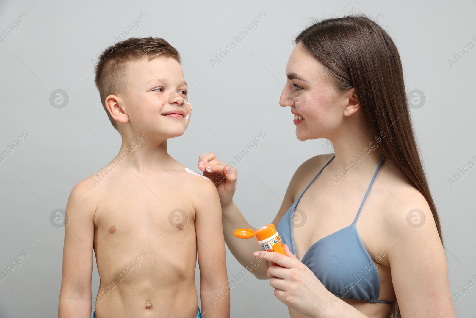Mother applying sun protection cream onto her son's skin on light grey background Photo of Mother applying sun protection cream onto her son's skin on light grey background