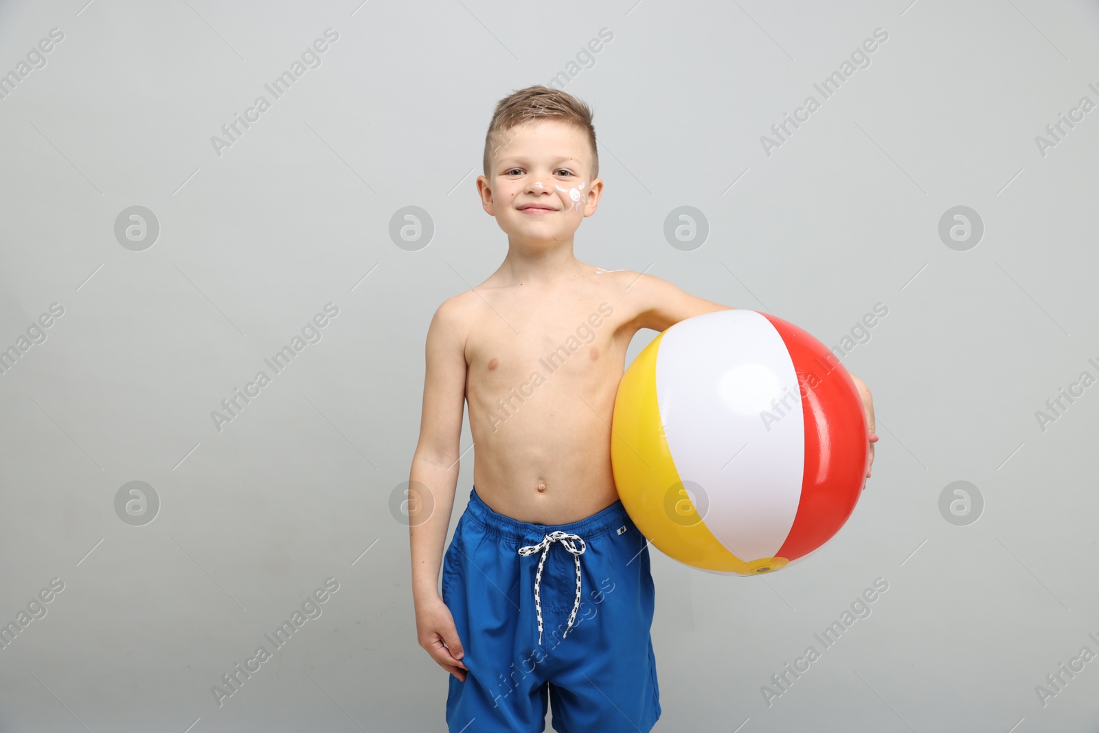 Little boy with sun protection cream on his skin and inflatable ball against light grey background Photo of Little boy with sun protection cream on his skin and inflatable ball against light grey background