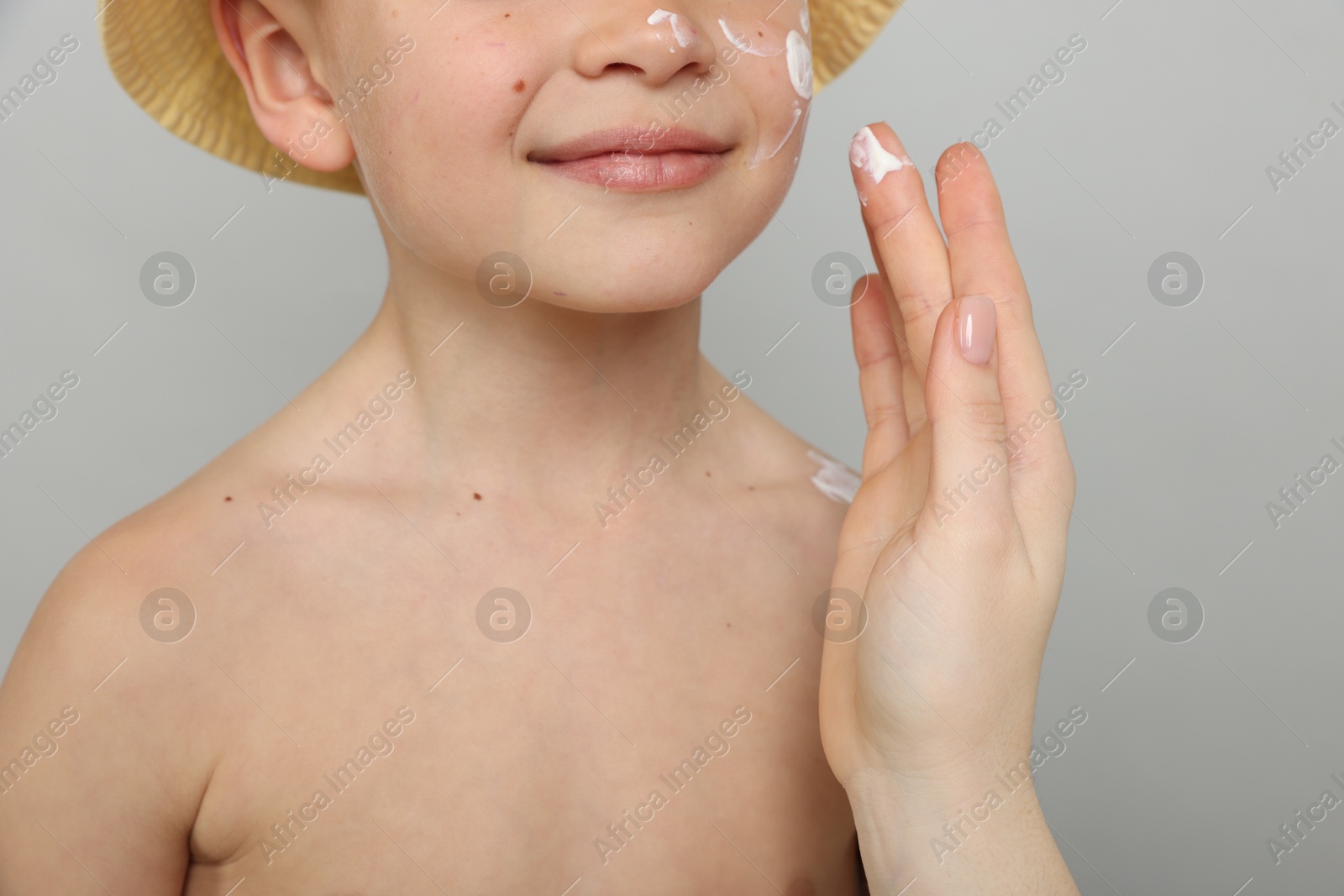 Mother applying sun protection cream onto her son's skin on light grey background, closeup Photo of Mother applying sun protection cream onto her son's skin on light grey background, closeup