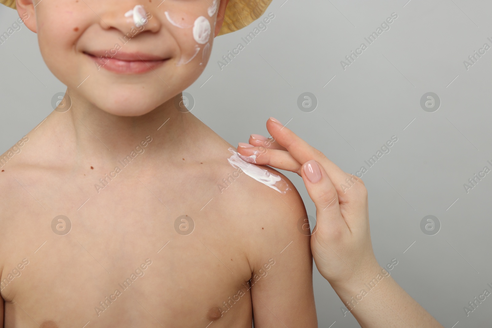 Mother applying sun protection cream onto her son's skin on light grey background, closeup Photo of Mother applying sun protection cream onto her son's skin on light grey background, closeup