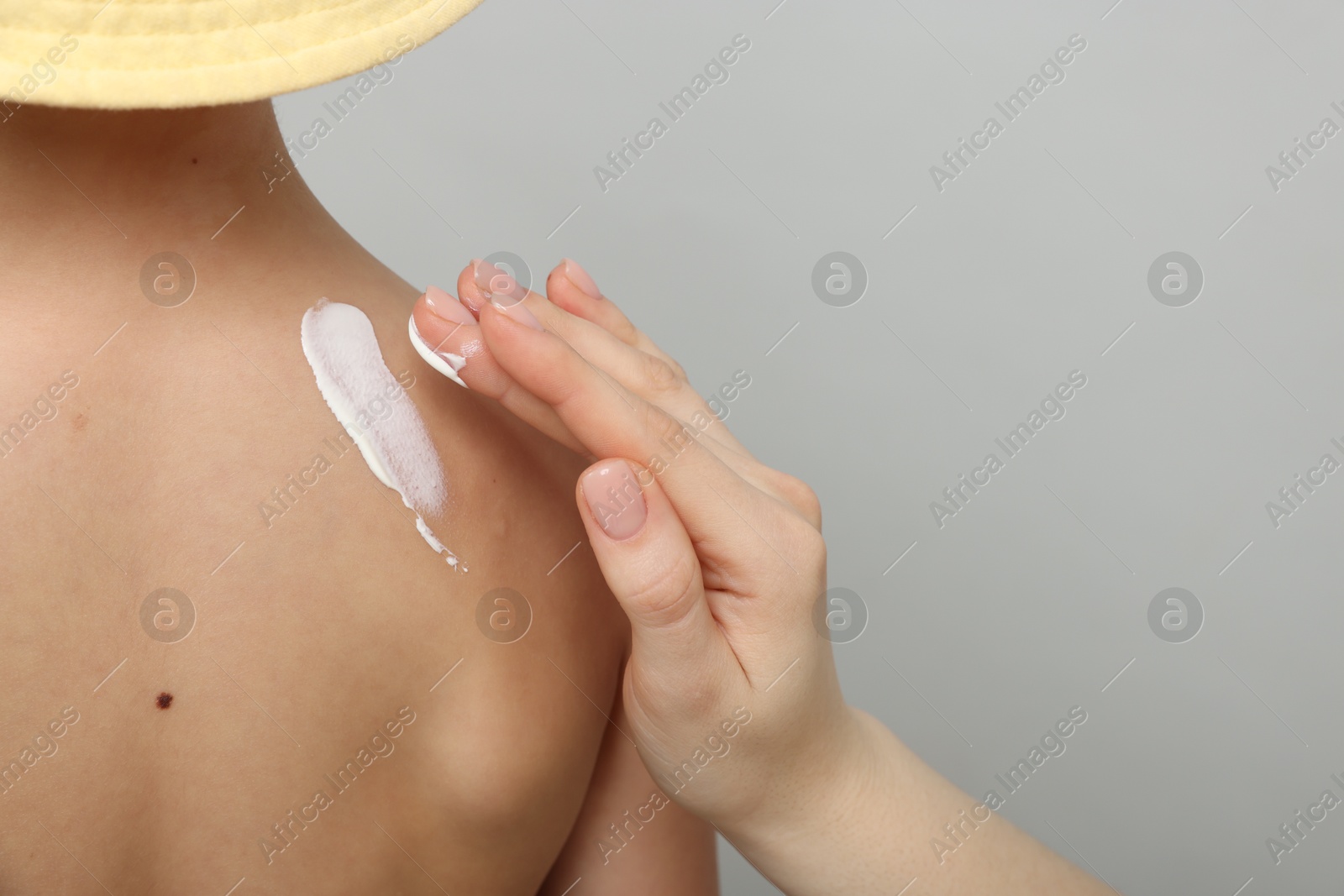 Mother applying sun protection cream onto her son's skin on light grey background, closeup. Space for text Photo of Mother applying sun protection cream onto her son's skin on light grey background, closeup. Space for text