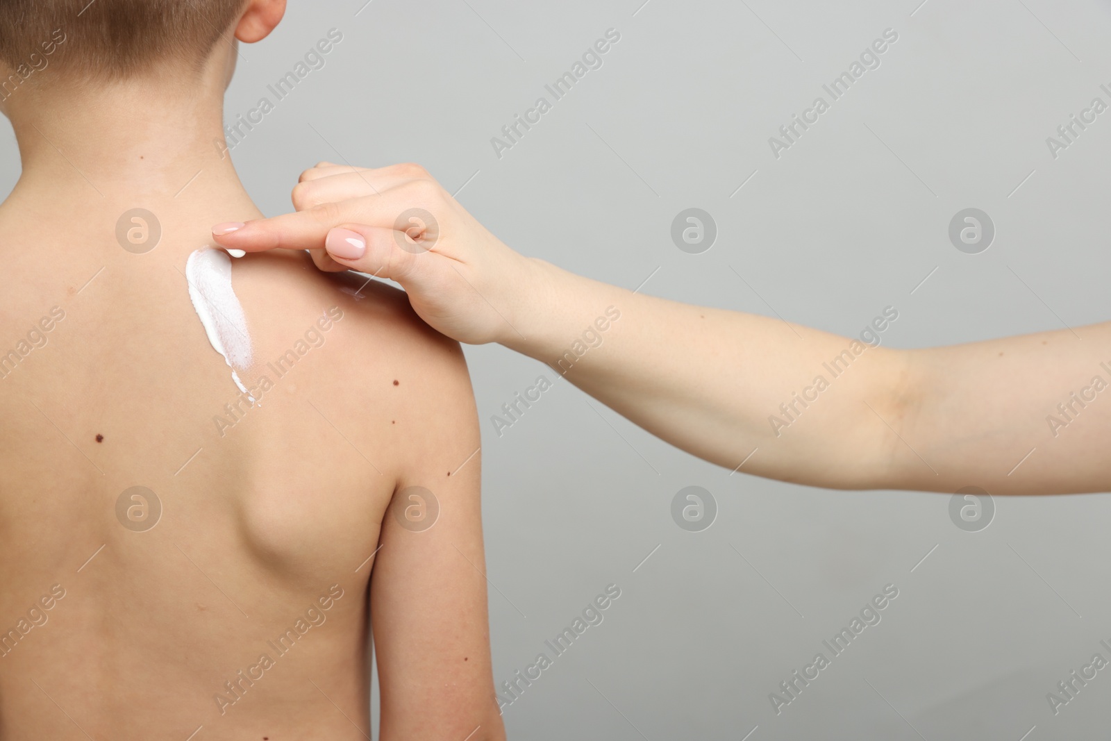 Mother applying sun protection cream onto her son's skin on light grey background, closeup Photo of Mother applying sun protection cream onto her son's skin on light grey background, closeup