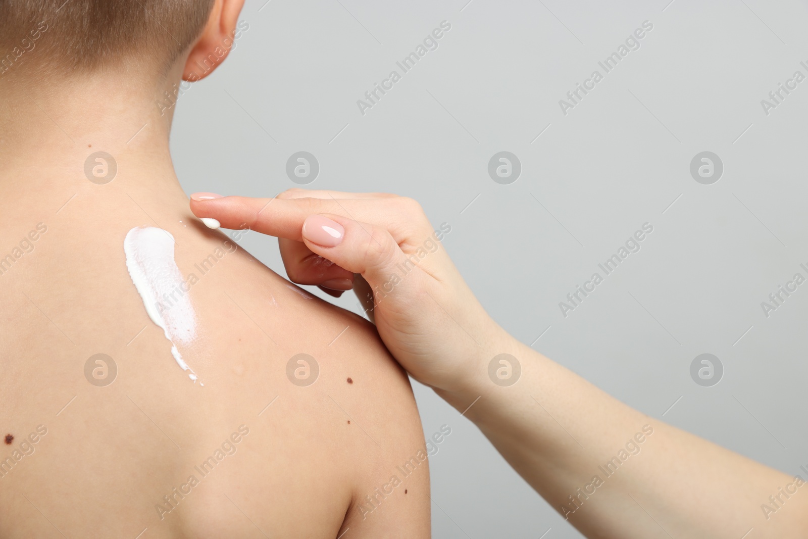 Mother applying sun protection cream onto her son's skin on light grey background, closeup Photo of Mother applying sun protection cream onto her son's skin on light grey background, closeup