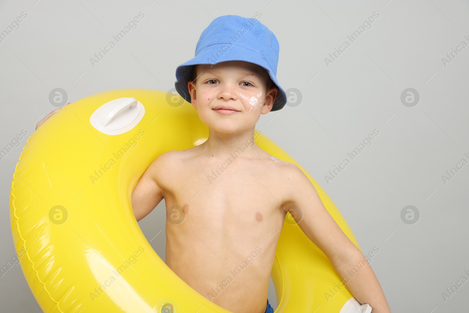 Little boy with sun protection cream on his skin and inflatable ring against light grey background Photo of Little boy with sun protection cream on his skin and inflatable ring against light grey background