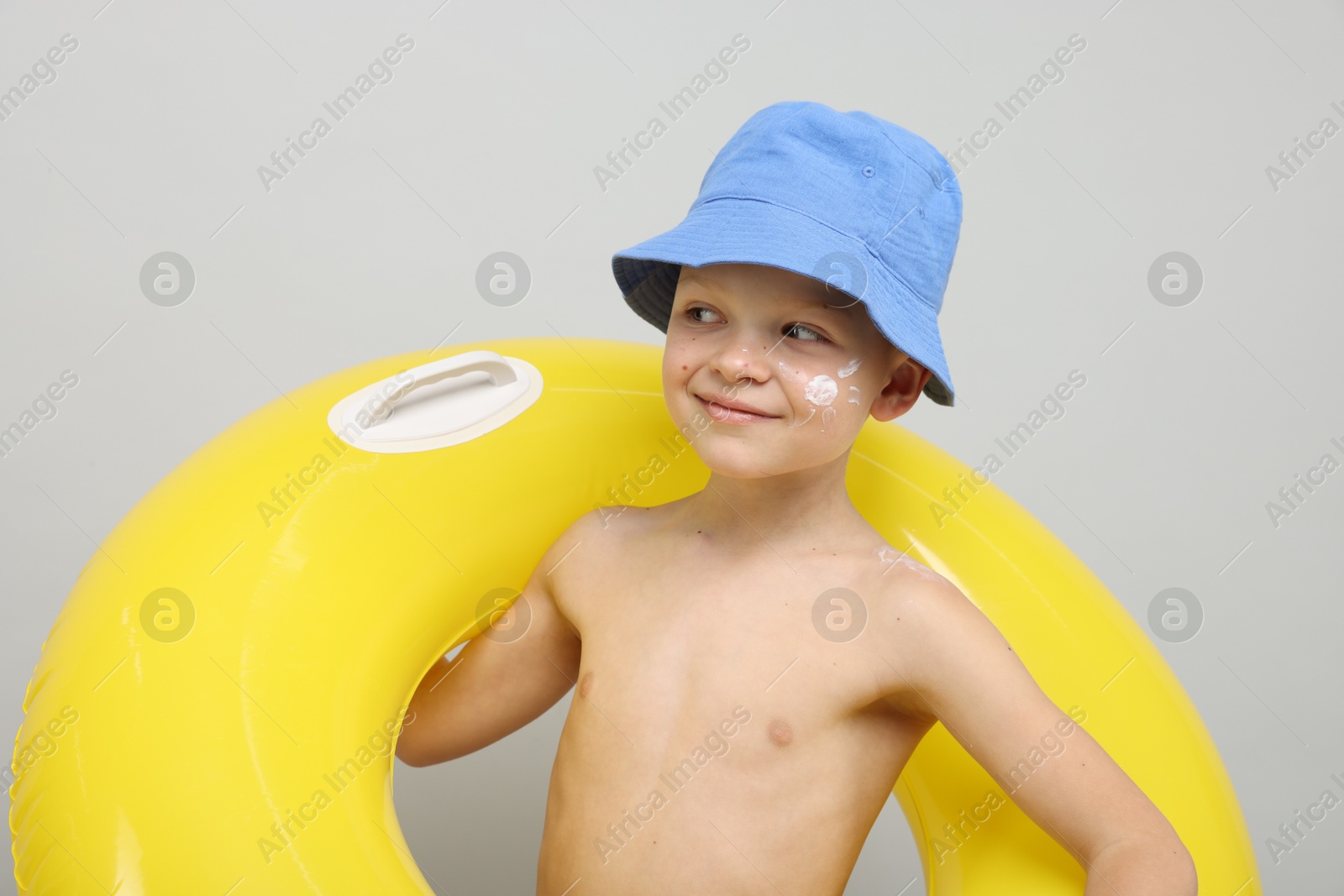 Little boy with sun protection cream on his skin and inflatable ring against light grey background Photo of Little boy with sun protection cream on his skin and inflatable ring against light grey background
