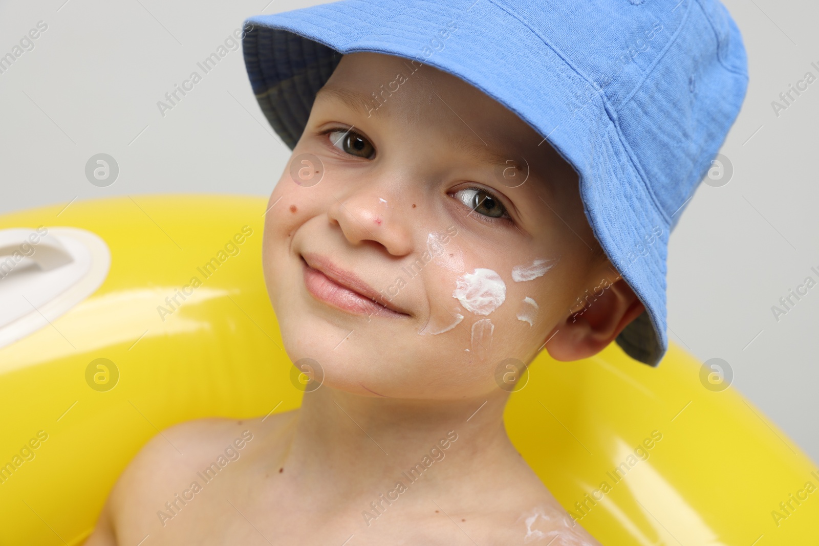 Little boy with sun protection cream on his skin and inflatable ring against light grey background Photo of Little boy with sun protection cream on his skin and inflatable ring against light grey background