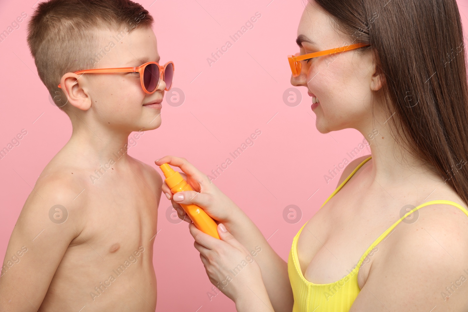 Mother applying sun protection cream onto her son's skin on pink background Photo of Mother applying sun protection cream onto her son's skin on pink background
