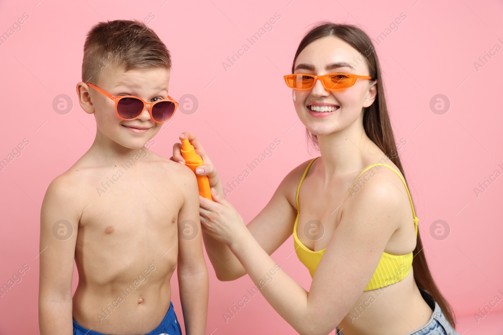 Mother applying sun protection cream onto her son's skin on pink background Photo of Mother applying sun protection cream onto her son's skin on pink background