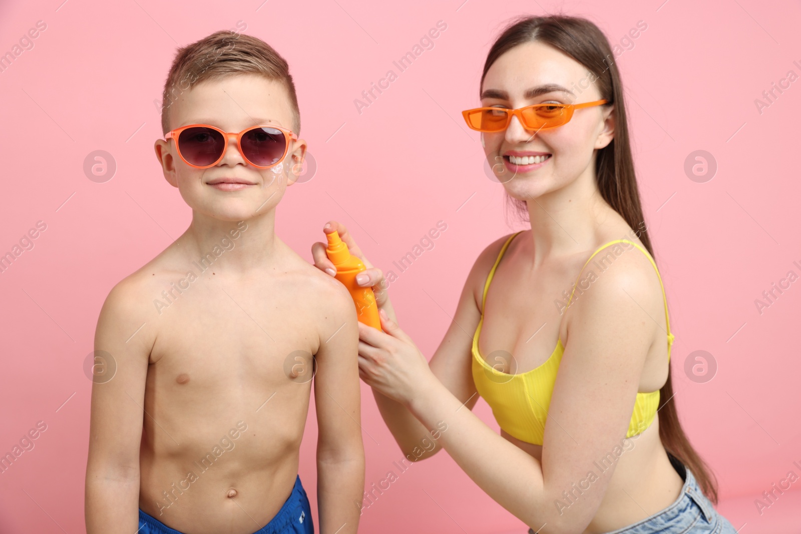Mother applying sun protection cream onto her son's skin on pink background Photo of Mother applying sun protection cream onto her son's skin on pink background