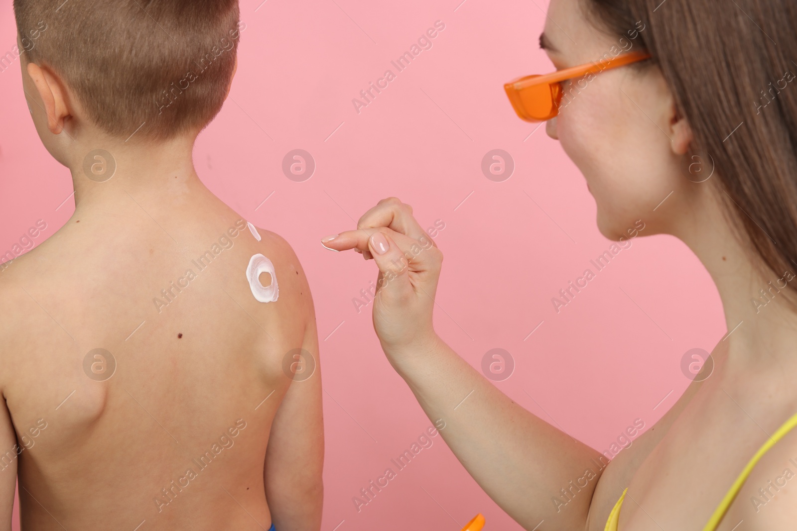 Mother applying sun protection cream onto her son's skin on pink background, closeup Photo of Mother applying sun protection cream onto her son's skin on pink background, closeup