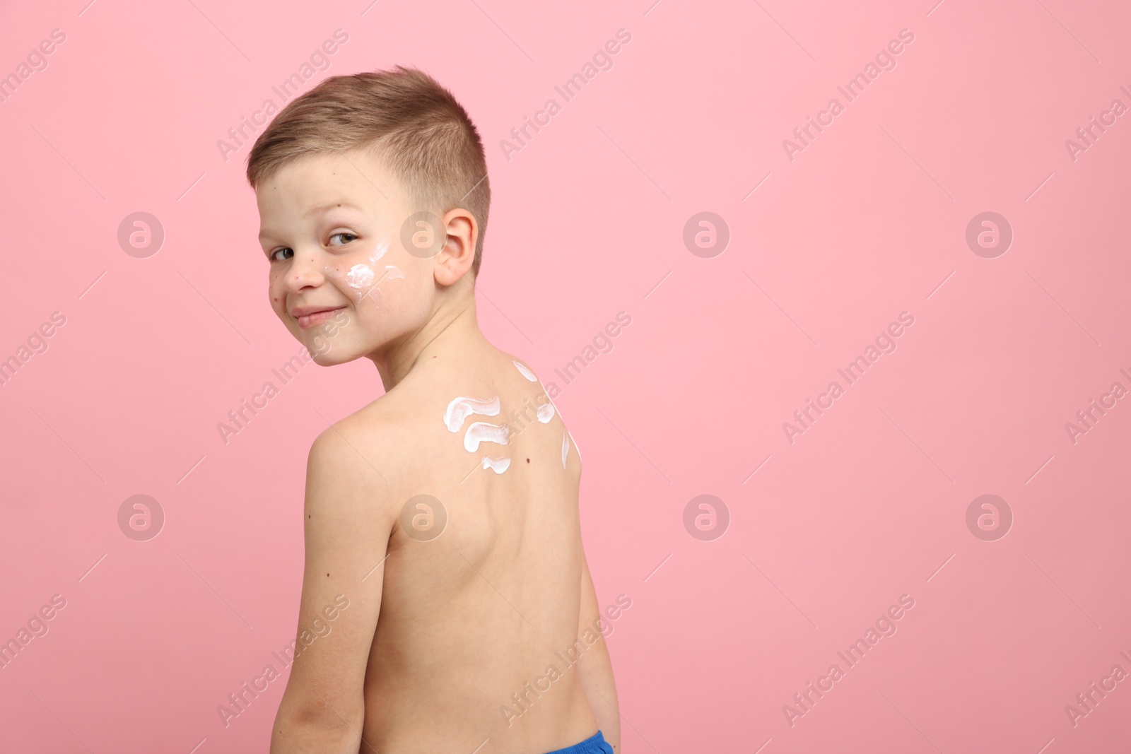 Little boy with sun protection cream on his skin against pink background, space for text Photo of Little boy with sun protection cream on his skin against pink background, space for text