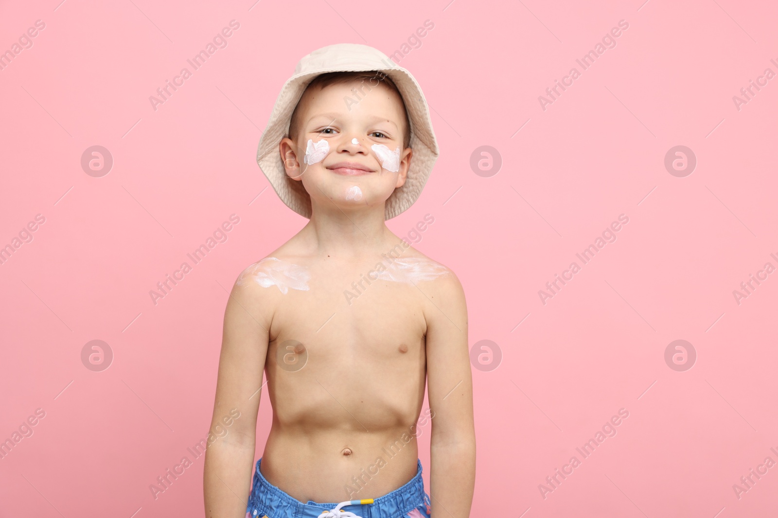 Photo of Little boy with sun protection cream on his skin against pink background