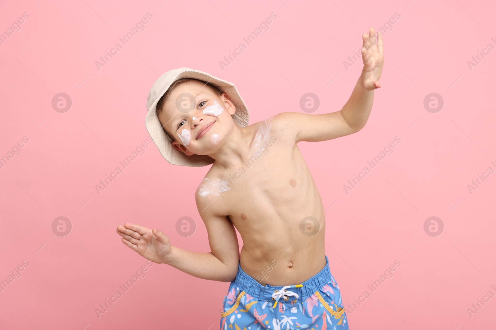 Photo of Little boy with sun protection cream on his skin against pink background