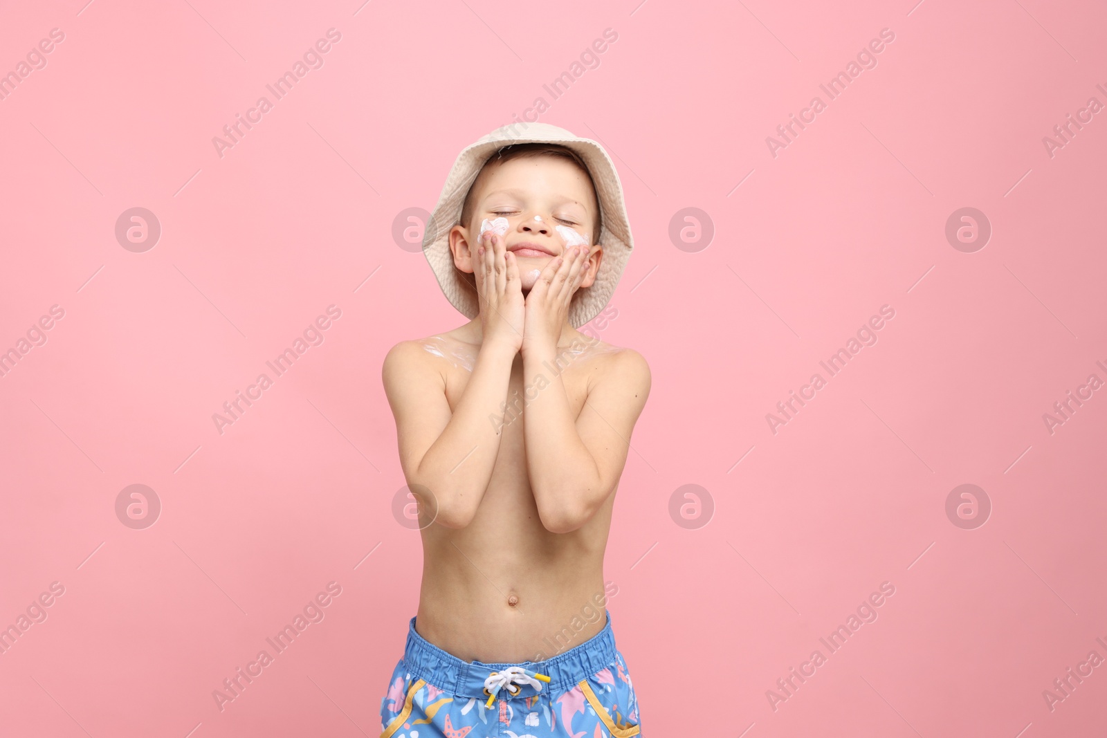 Photo of Little boy applying sun protection cream onto his skin on pink background
