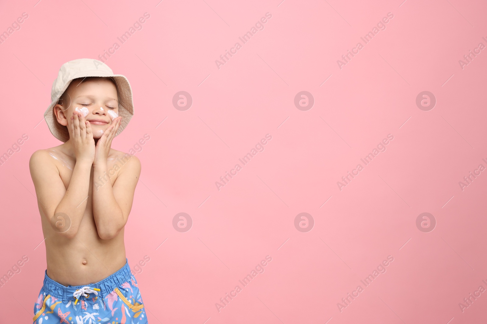 Little boy applying sun protection cream onto his skin on pink background, space for text Photo of Little boy applying sun protection cream onto his skin on pink background, space for text