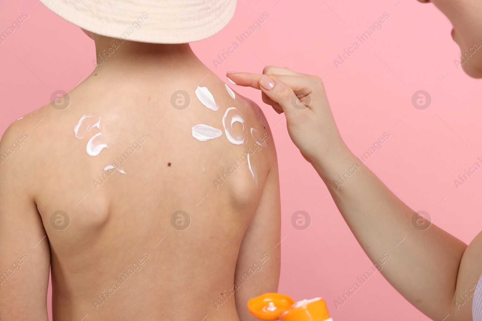 Mother applying sun protection cream onto her son's skin on pink background, closeup Photo of Mother applying sun protection cream onto her son's skin on pink background, closeup
