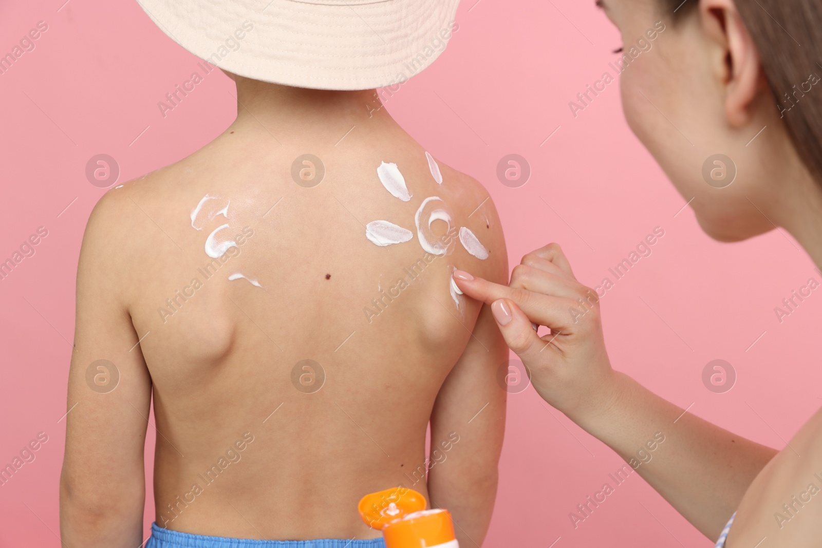 Mother applying sun protection cream onto her son's skin on pink background, closeup Photo of Mother applying sun protection cream onto her son's skin on pink background, closeup