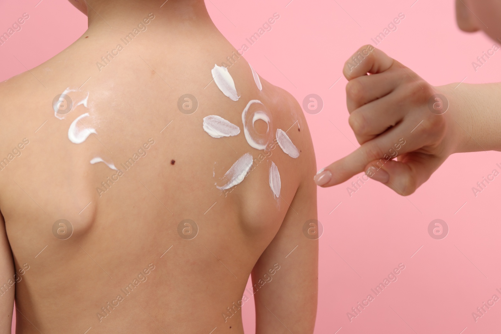 Mother applying sun protection cream onto her son's skin on pink background, closeup Photo of Mother applying sun protection cream onto her son's skin on pink background, closeup