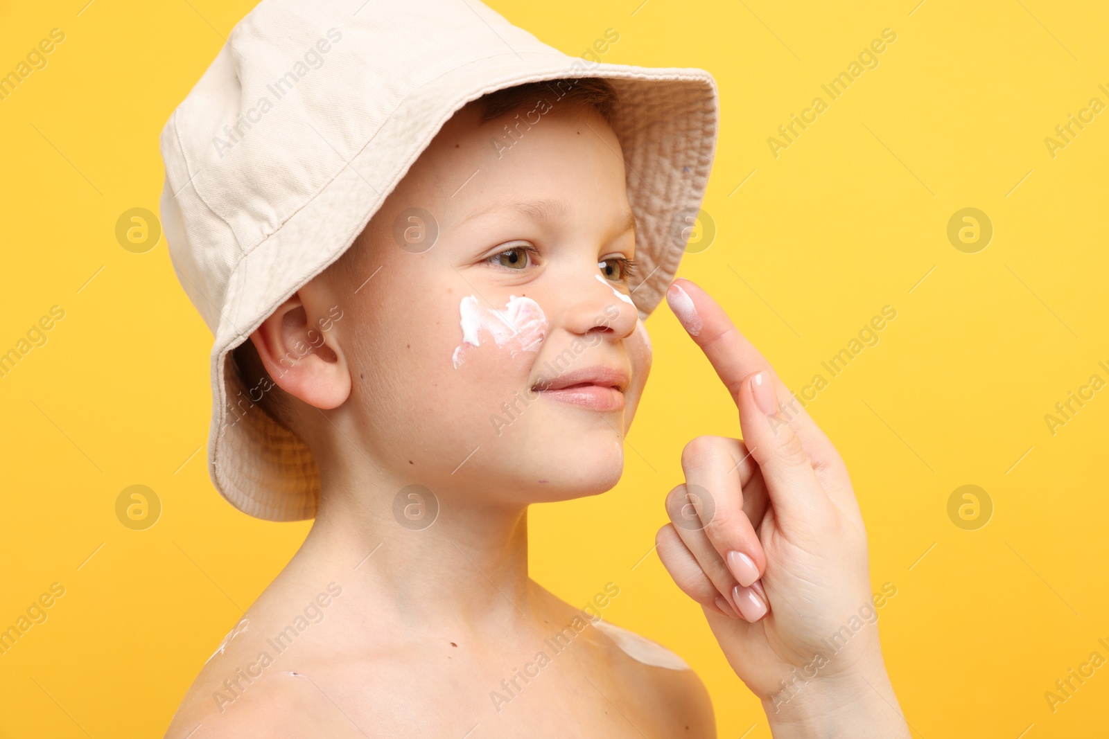 Mother applying sun protection cream onto her son's skin on yellow background, closeup Photo of Mother applying sun protection cream onto her son's skin on yellow background, closeup