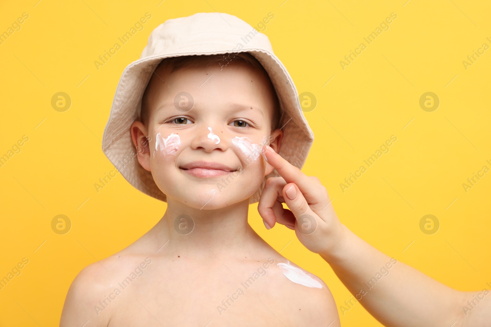 Mother applying sun protection cream onto her son's skin on yellow background, closeup Photo of Mother applying sun protection cream onto her son's skin on yellow background, closeup