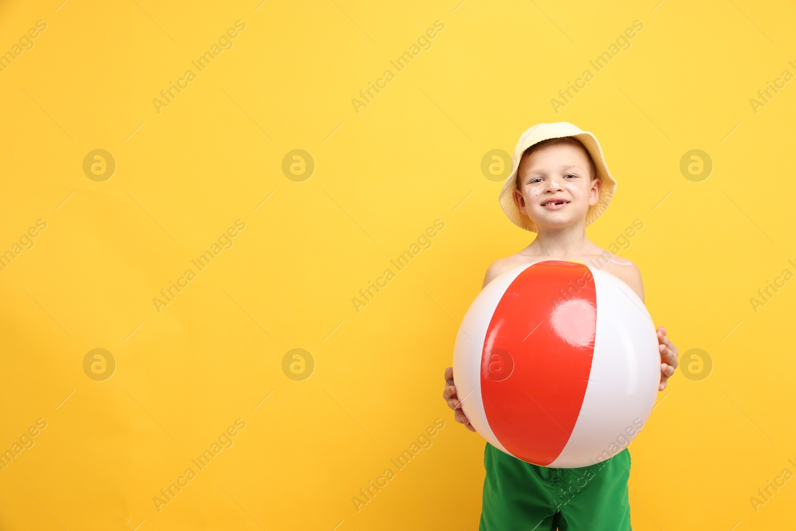 Little boy with sun protection cream on his skin and inflatable ball against yellow background, space for text Photo of Little boy with sun protection cream on his skin and inflatable ball against yellow background, space for text