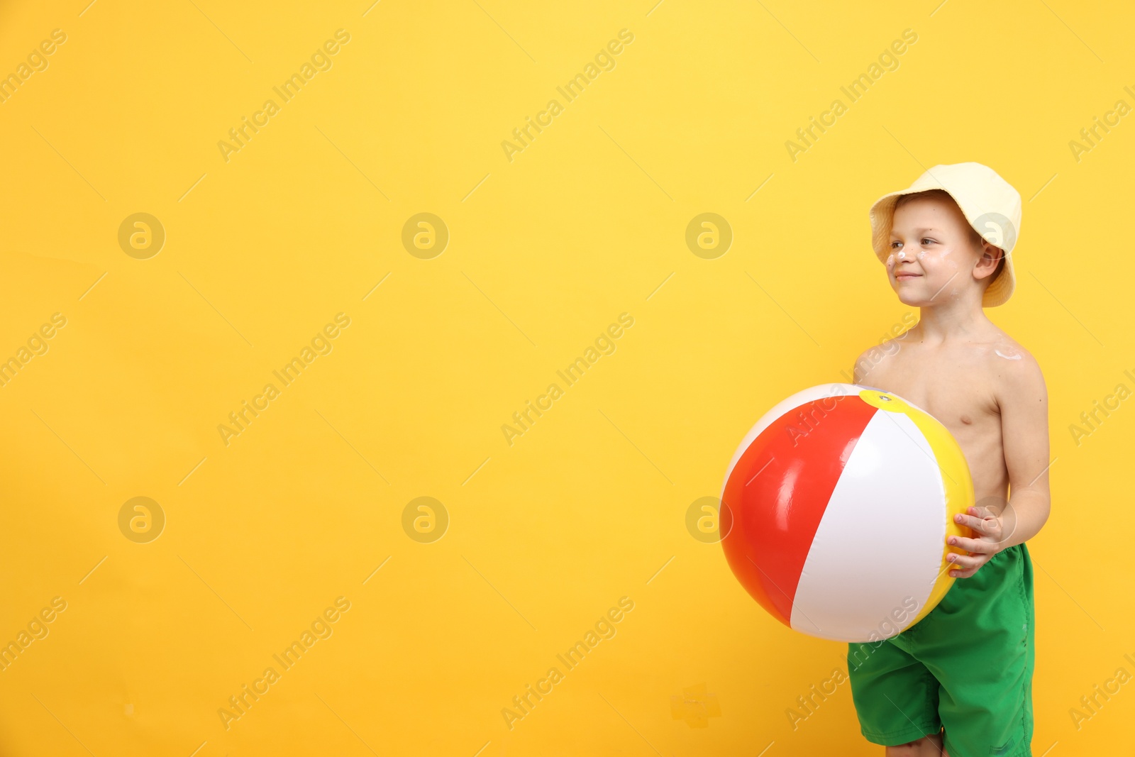 Little boy with sun protection cream on his skin and inflatable ball against yellow background, space for text Photo of Little boy with sun protection cream on his skin and inflatable ball against yellow background, space for text