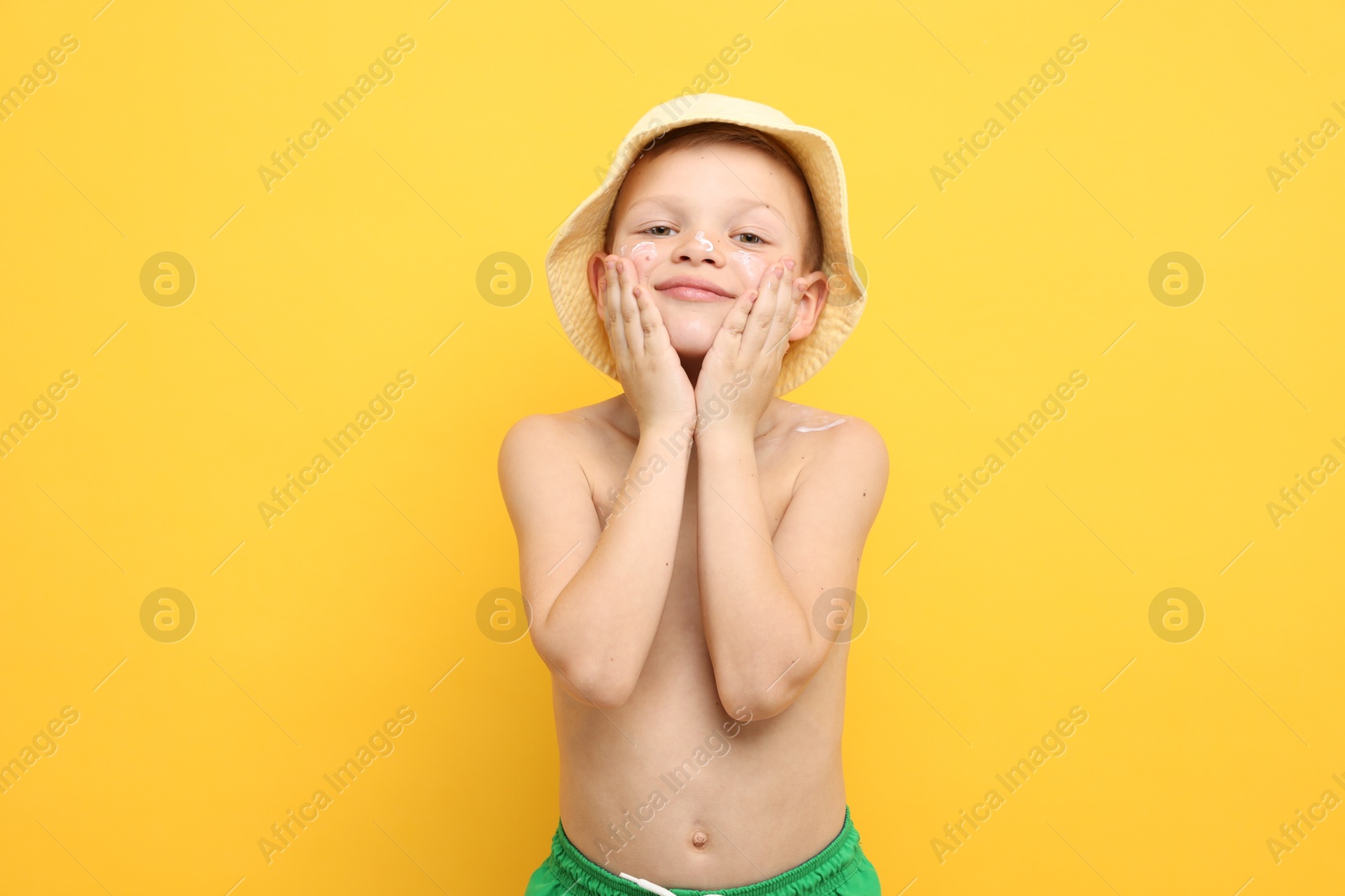 Little boy applying sun protection cream onto his skin on yellow background Photo of Little boy applying sun protection cream onto his skin on yellow background