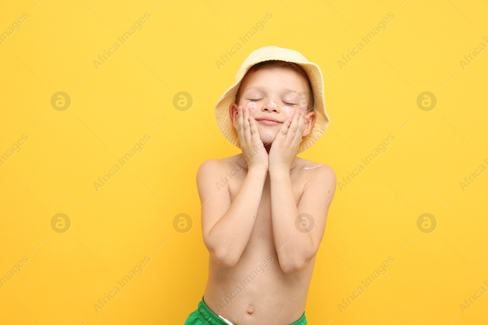 Little boy applying sun protection cream onto his skin on yellow background Photo of Little boy applying sun protection cream onto his skin on yellow background