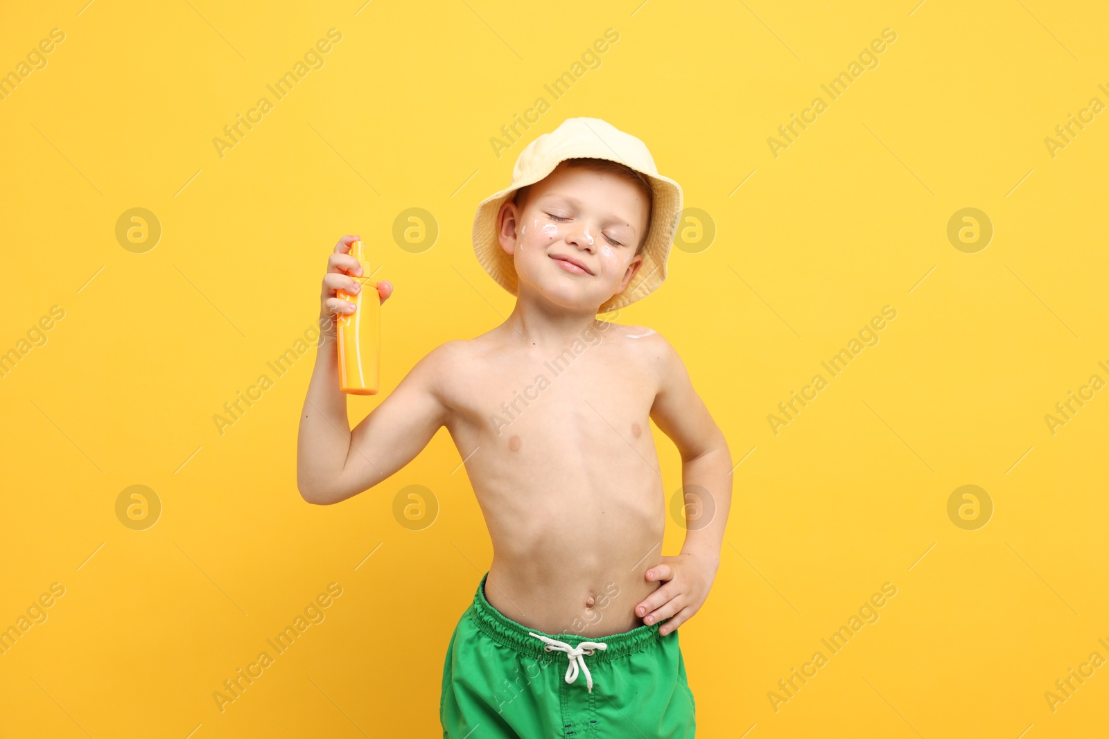 Little boy with tube of sun protection cream on yellow background Photo of Little boy with tube of sun protection cream on yellow background