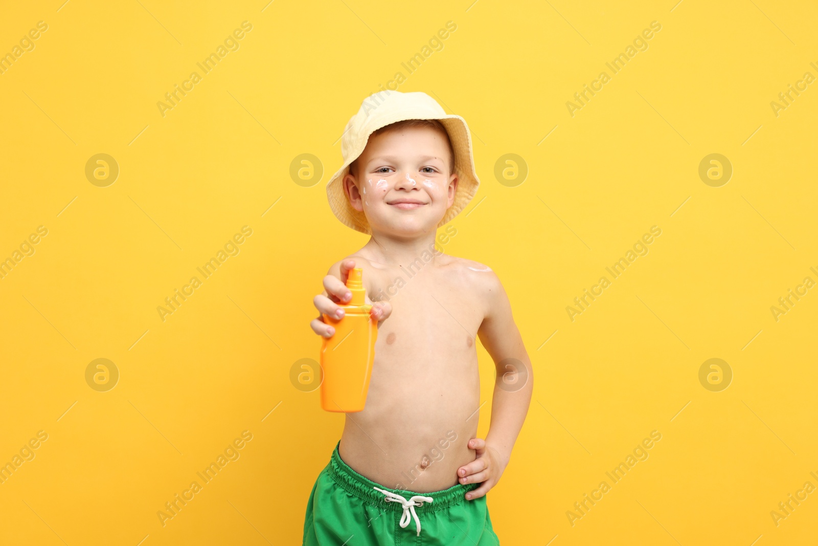 Little boy with tube of sun protection cream on yellow background Photo of Little boy with tube of sun protection cream on yellow background