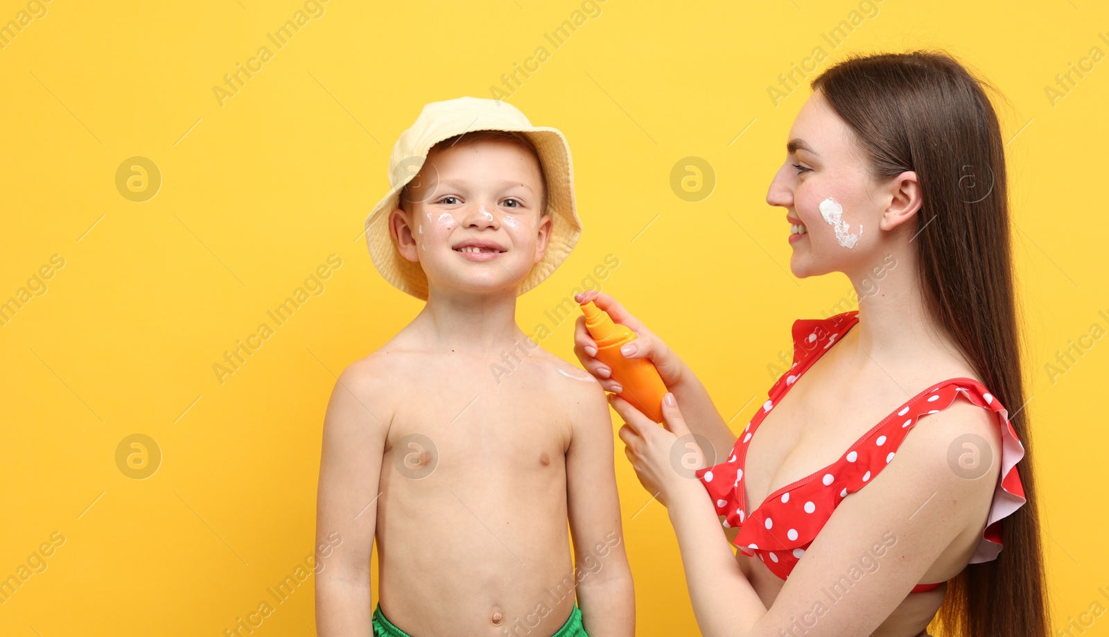 Mother applying sun protection cream onto her son's skin on yellow background Photo of Mother applying sun protection cream onto her son's skin on yellow background