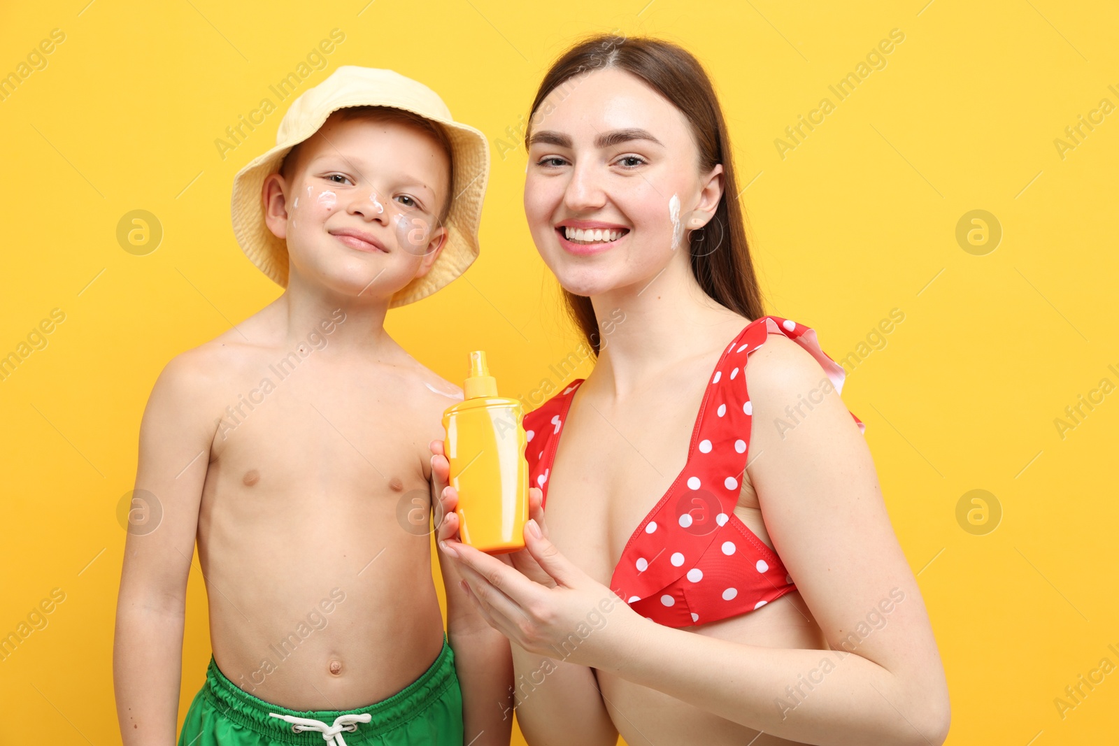 Mother with sun protection cream and her son on yellow background Photo of Mother with sun protection cream and her son on yellow background