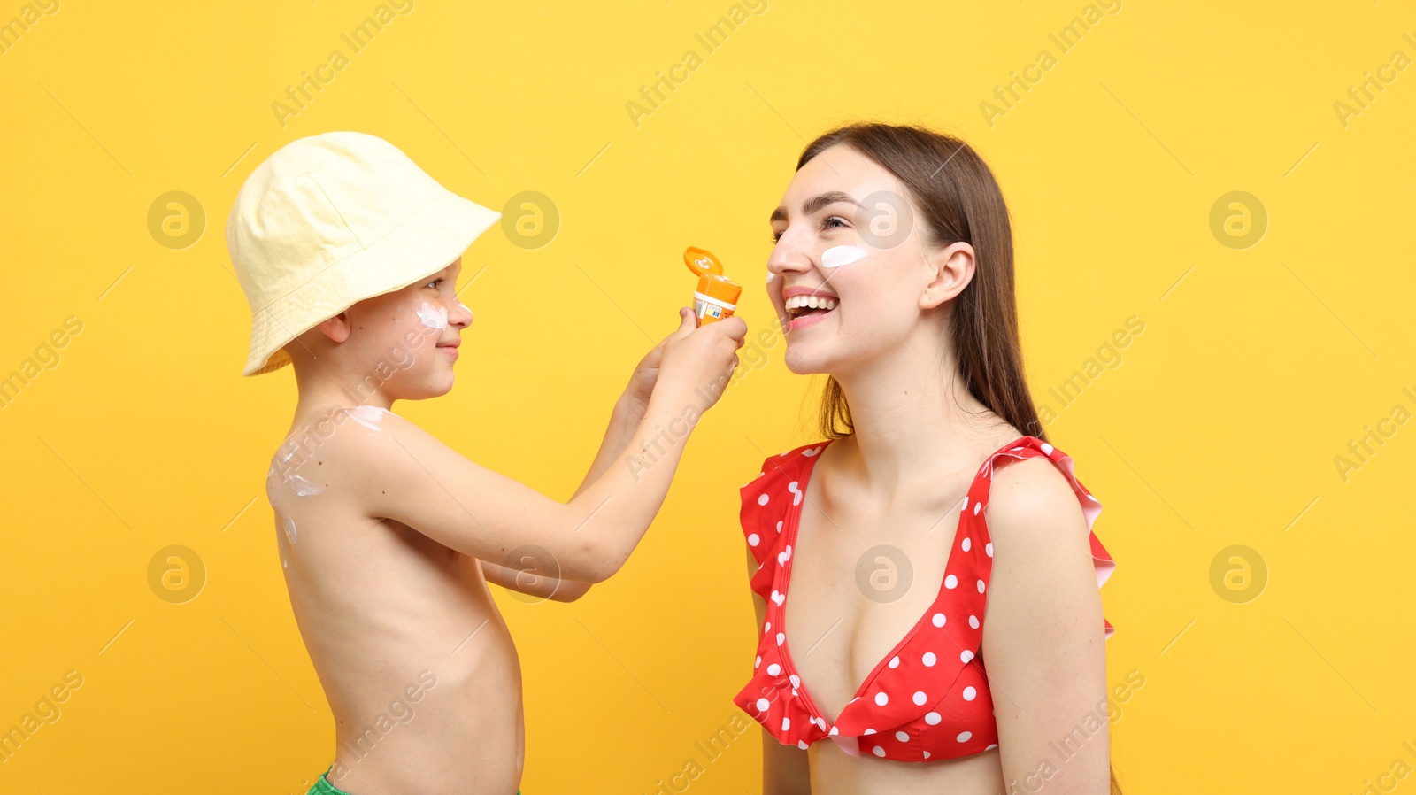 Son applying sun protection cream onto his mother's skin on yellow background Photo of Son applying sun protection cream onto his mother's skin on yellow background