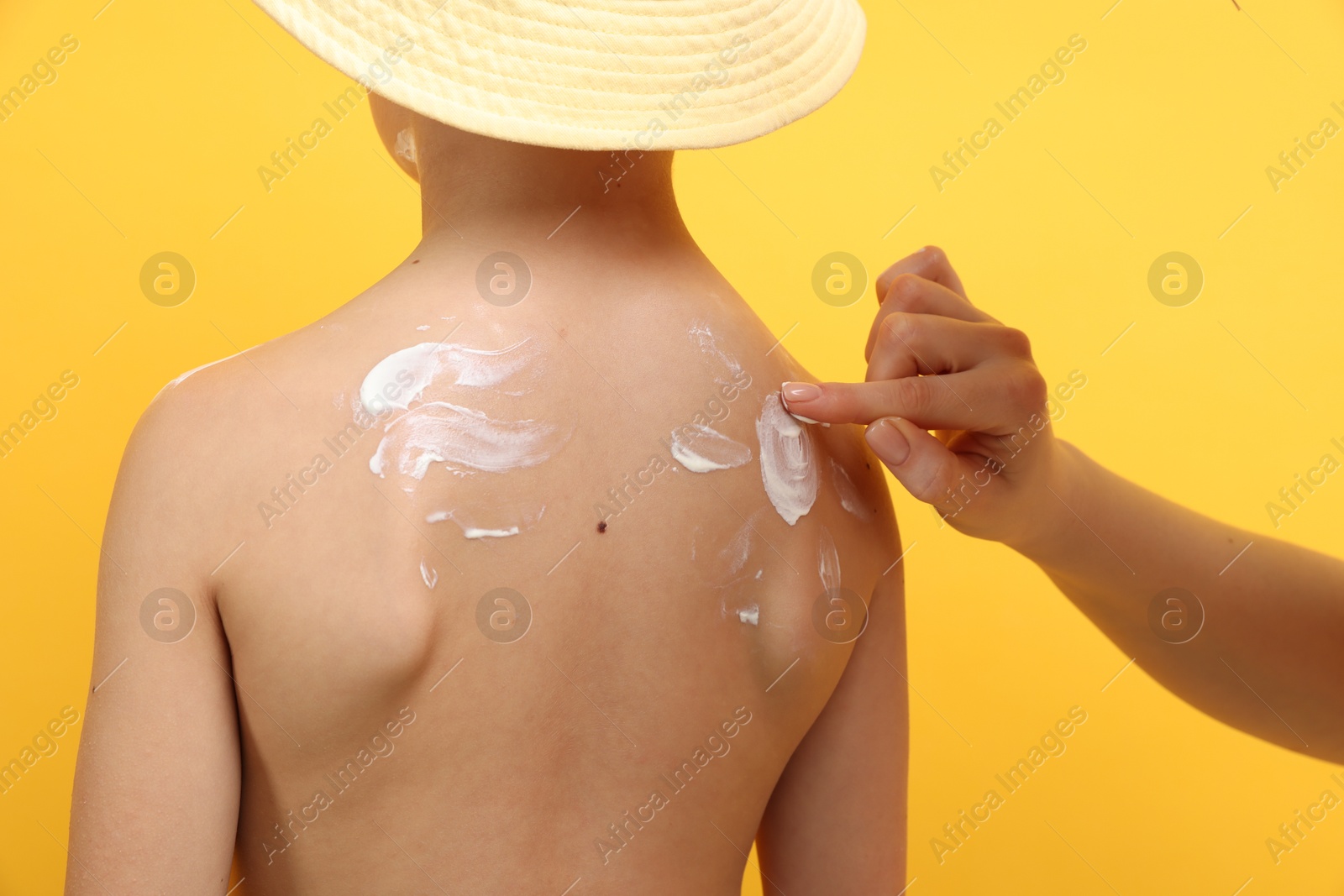 Mother applying sun protection cream onto her son's skin on yellow background, closeup Photo of Mother applying sun protection cream onto her son's skin on yellow background, closeup